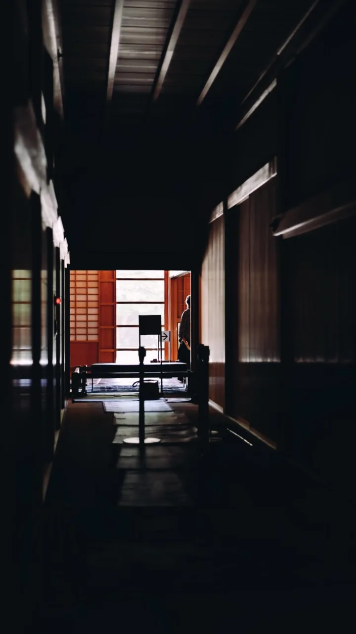 昏暗木造廊道通往明亮窗邊，縱深處留有一個人影。